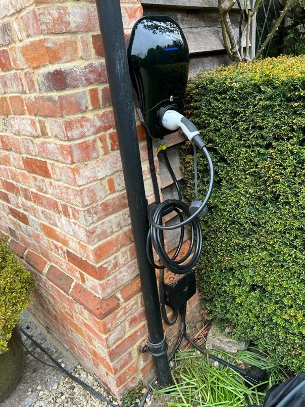 EV charger on a brick wall by a hedge